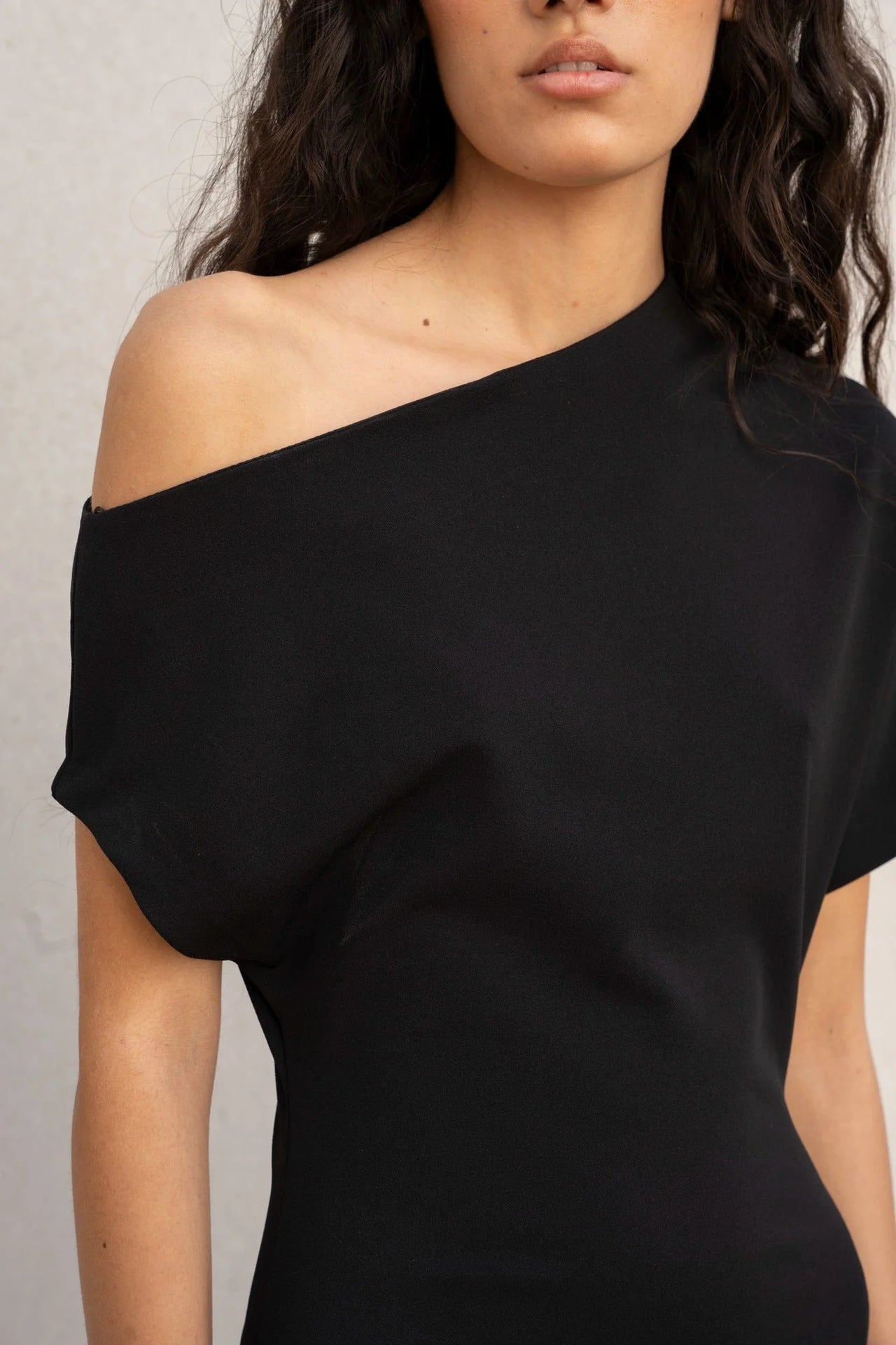 Détail de la robe asymétrique noire à épaule dénudée chic moulante midi pour soirée élégante, soulignant la coupe élégante et féminine.