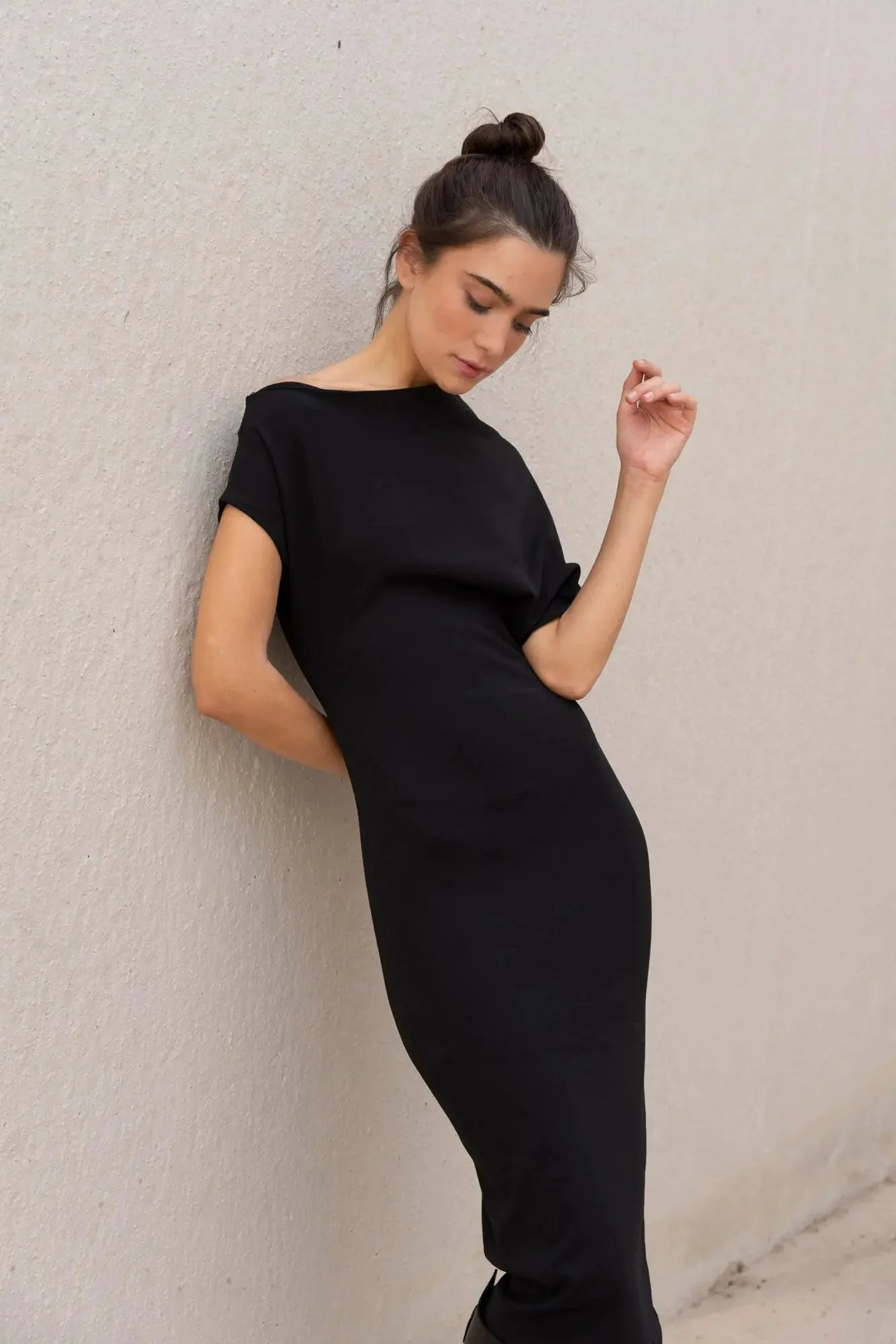Femme posant dans une robe asymétrique noire à épaule dénudée chic moulante midi pour soirée élégante, affichant un style minimaliste et féminin.