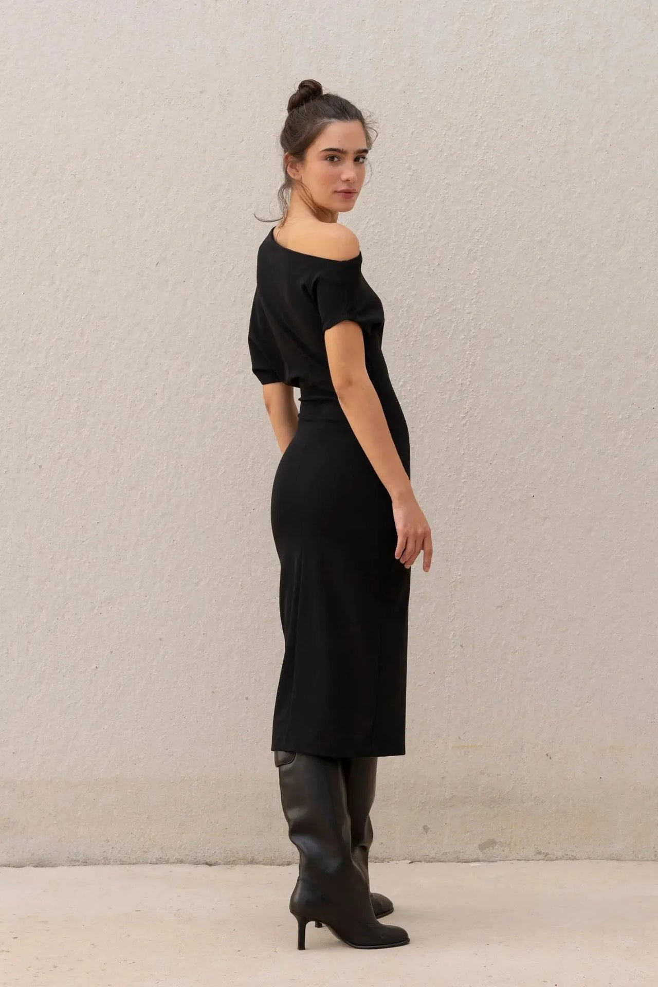 Femme en robe asymétrique noire à épaule dénudée chic moulante midi pour soirée élégante, montrant un style chic et sophistiqué.