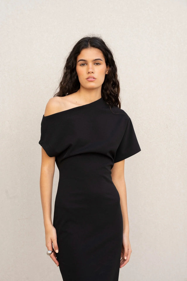 Vue frontale d'un modèle portant une robe asymétrique noire à épaule dénudée chic moulante midi pour soirée élégante, avec un regard captivant.