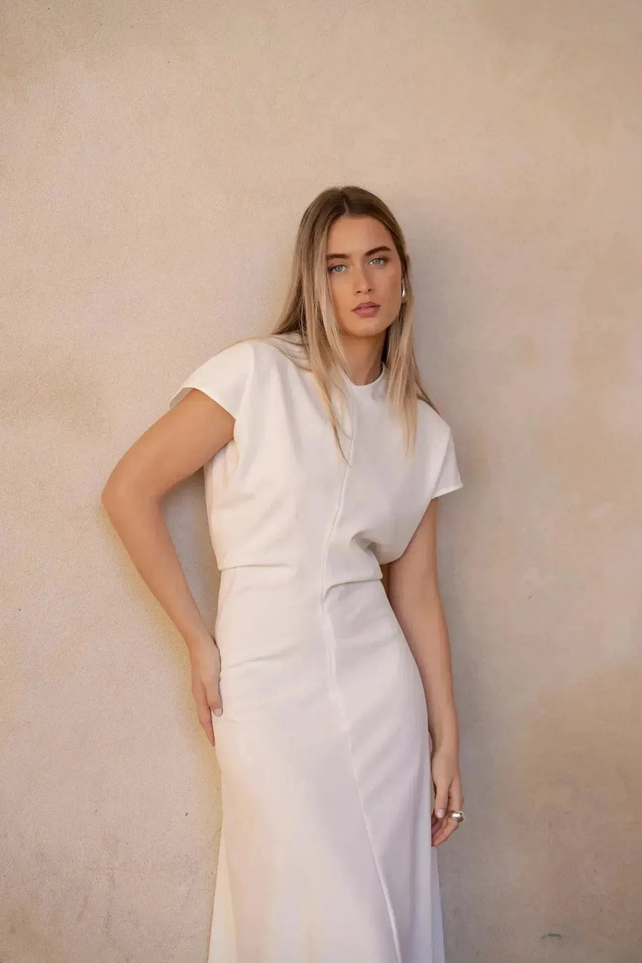 Jeune femme posant avec élégance dans une robe longue blanche chic à manches courtes, mettant en avant le design plissé élégant.