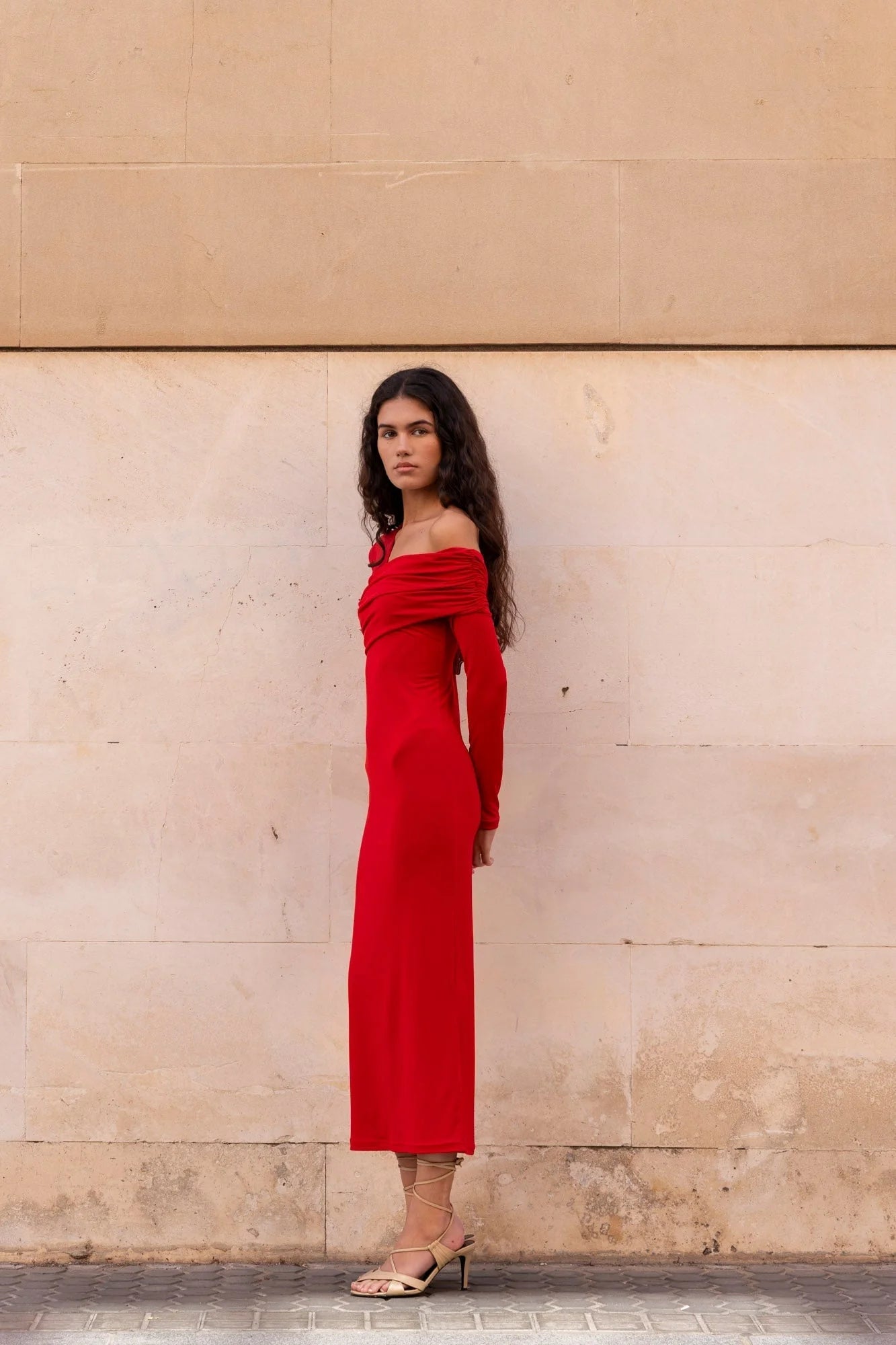 Robe Rouge Moulante Asymétrique à Épaules Découvertes | Modèle en profil, affichant la coupe élégante et la silhouette moderne de la robe rouge moulante.