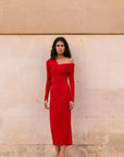 Robe Rouge Moulante Asymétrique à Épaules Découvertes | Modèle en rouge moulant devant un mur, parfaite pour vos soirées élégantes.