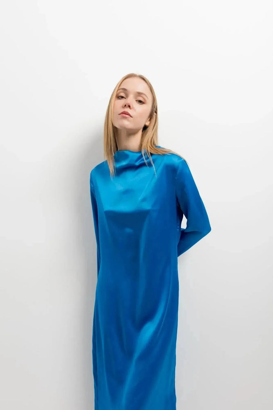 Gros plan d'une femme avec une robe satinée bleu électrique, col montant, manches longues, highlight sur le tissu satiné qui définit la robe satin longue.