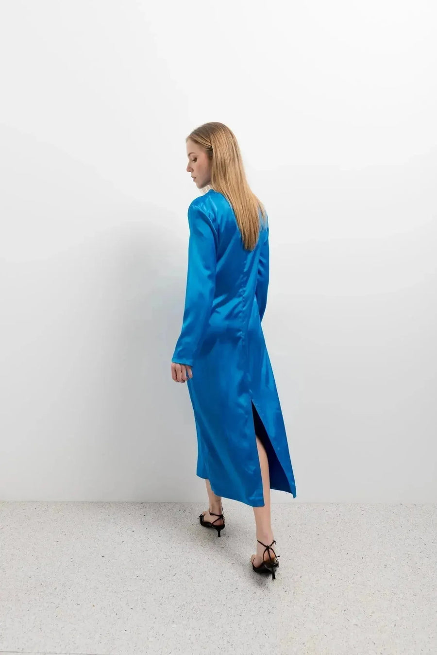 Vue arrière d'une femme portant une robe satinée bleu électrique avec une fente, illustrant le design élégant de cette robe satin longue.