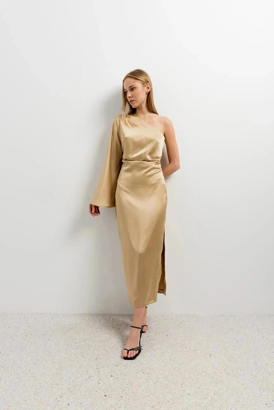 Modèle portant la Robe Dorée Satinée Asymétrique Une Manche, avec fente latérale, sur un fond sobre, parfaite pour les occasions spéciales.