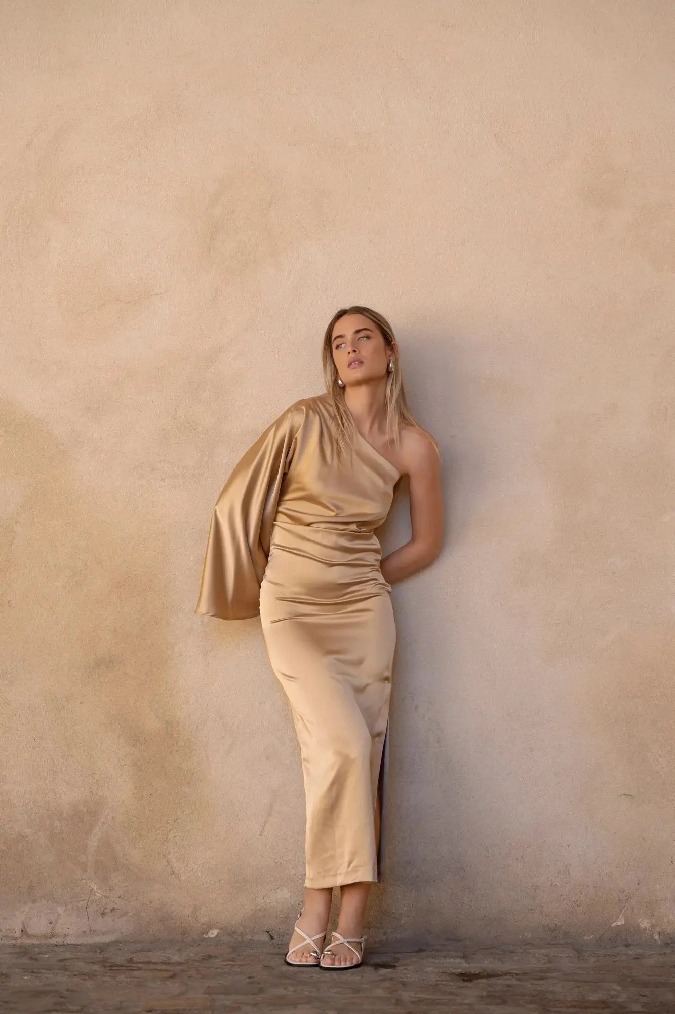 Jeune femme posant avec la Robe Dorée Satinée Asymétrique Une Manche Avec Fente Latérale, mettant en valeur son élégance pour soirées chic.
