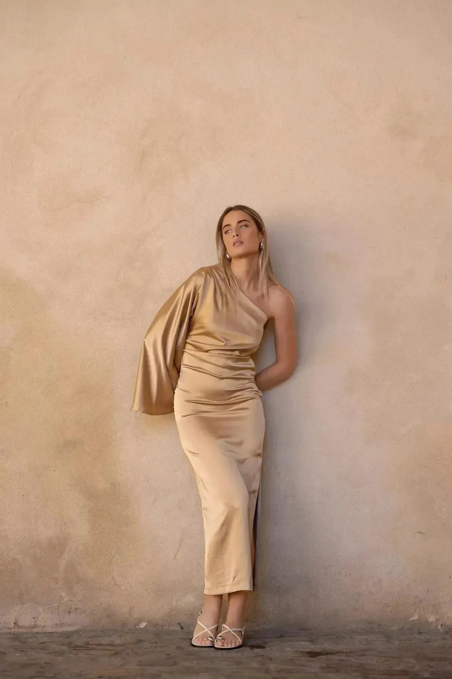 Jeune femme posant avec la Robe Dorée Satinée Asymétrique Une Manche Avec Fente Latérale, mettant en valeur son élégance pour soirées chic.