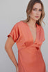 Femme portant une robe midi satinée orange cuivré avec décolleté cache-cœur, mettant en valeur le tissu léger et l'éclat de la robe satin orange.