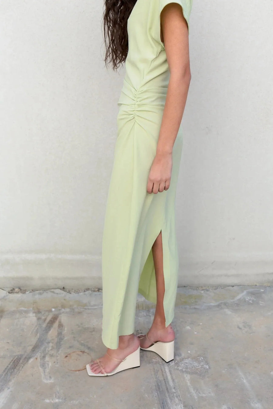 Femme en robe verte pastel midi plissée avec fente, dégageant une allure élégante pour diverses occasions.