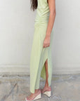 Femme en robe verte pastel midi plissée avec fente, dégageant une allure élégante pour diverses occasions.