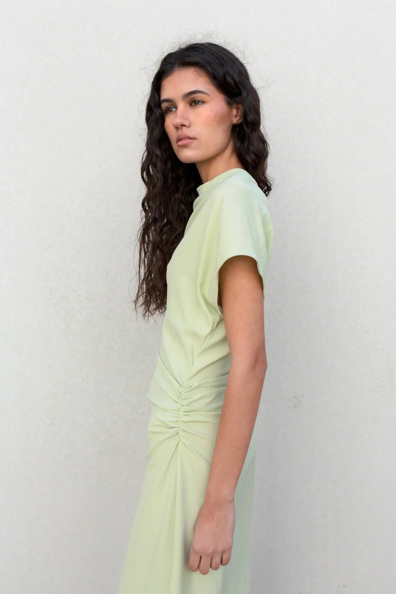 Femme portant une robe midi verte claire avec jupe froncée, style élégant et trendy