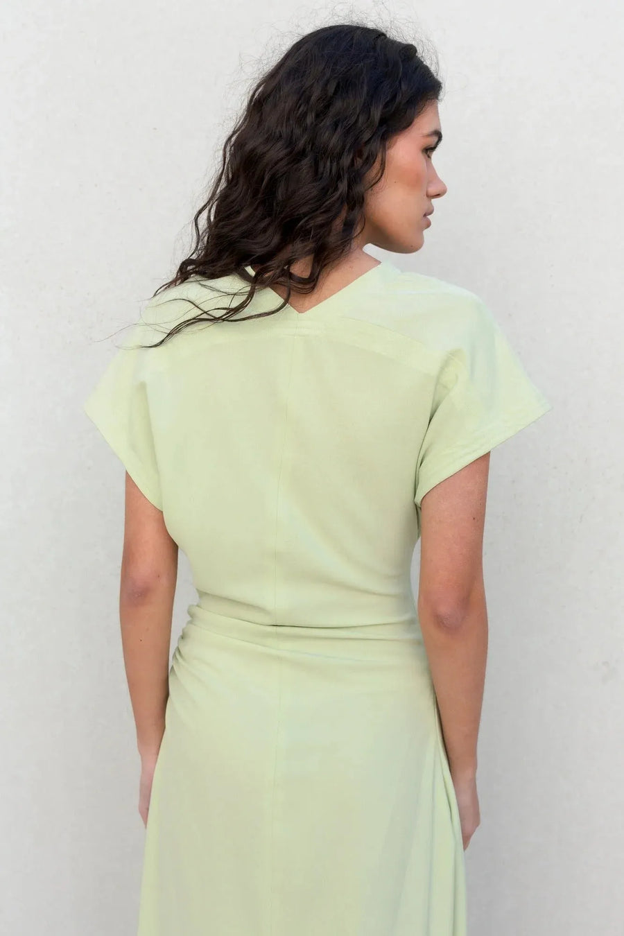 Vue arrière d'une robe verte pastel midi plissée avec fente, illustrant la coupe flatteuse et élégante.