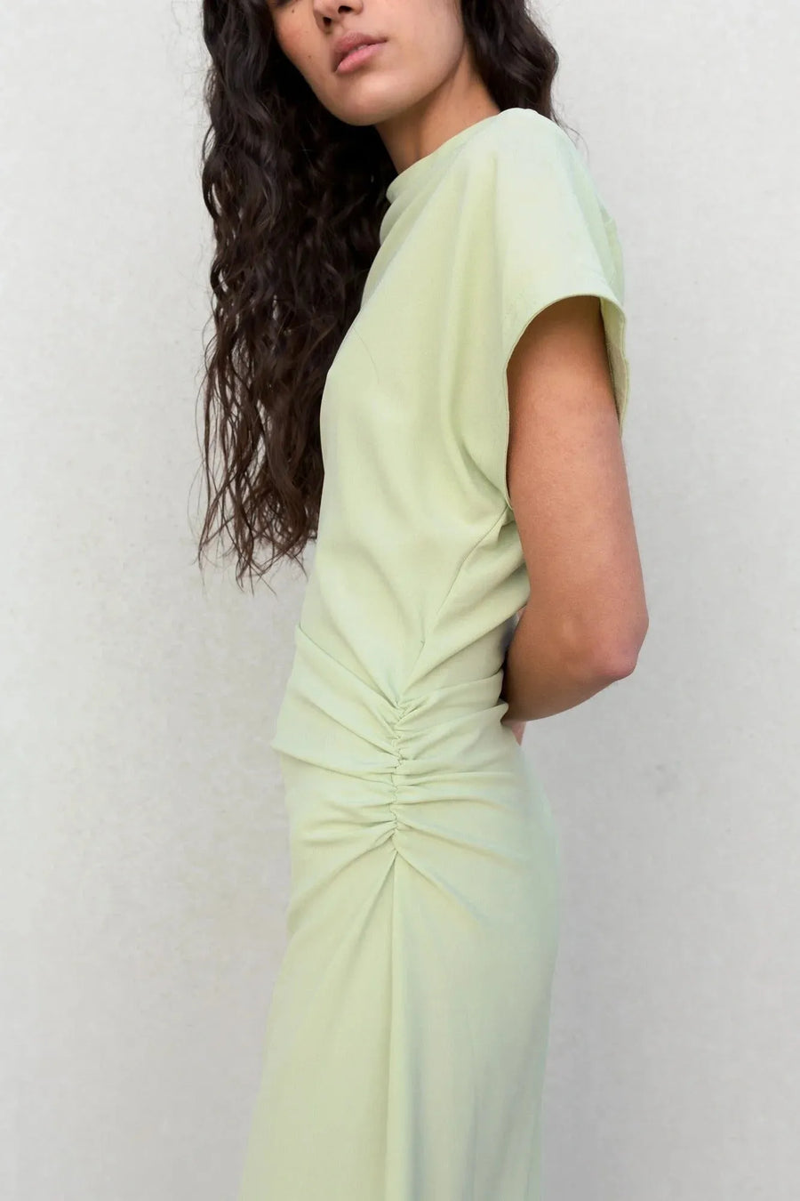 Profil d'une robe verte pastel midi plissée avec fente, soulignant la texture plissée et le design tendance.