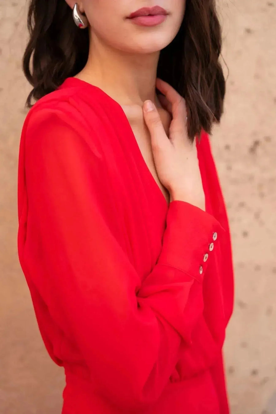 Détail sur la robe mousseline rouge midi, mettant en avant le décolleté plongeant et les manches longues élégantes.