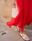 Femme marchant avec une robe mousseline rouge midi et des sandales, mettant en valeur la fluidité de la robe à décolleté plongeant.