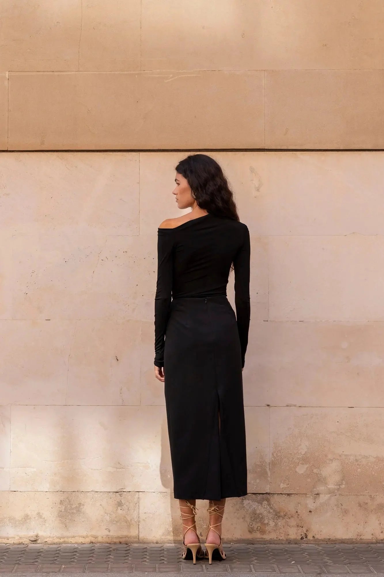 Femme portant une robe noire à épaulettes et jupe midi fendue avec talons dorés