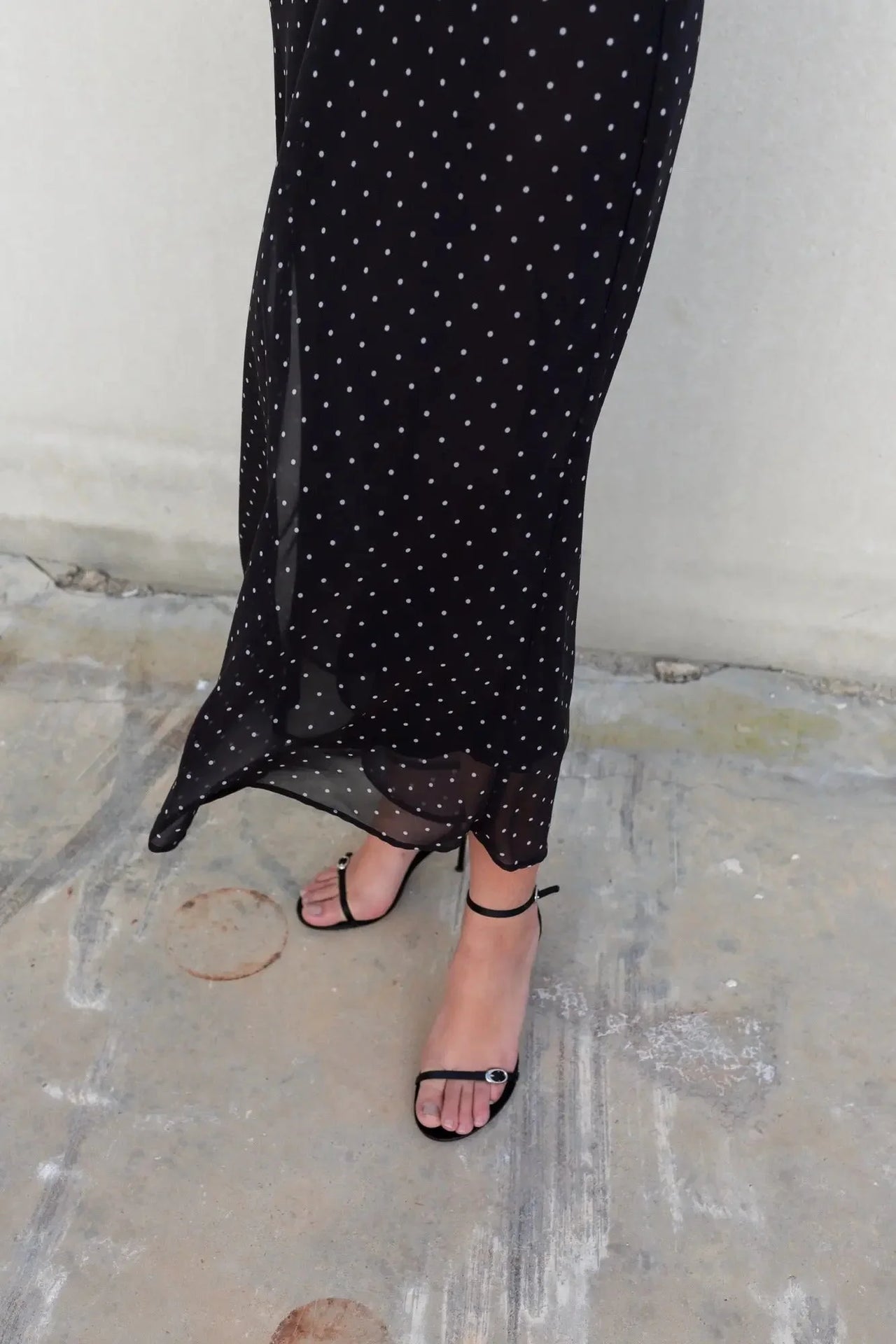 Femme portant la robe noire à pois blanc, avec une vue arrière qui met en avant le design élégant et contemporain.