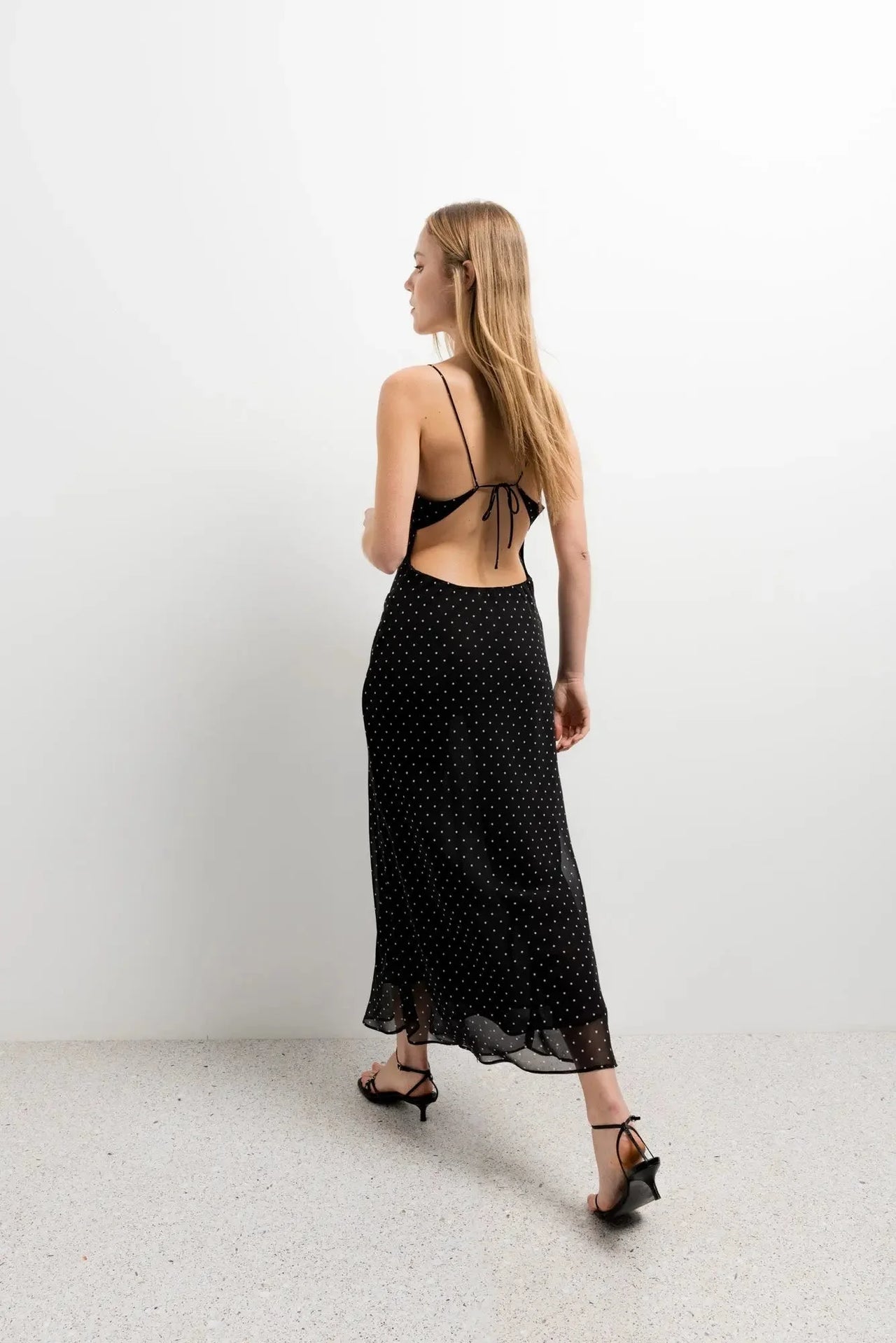 Vue arrière de la robe noire à pois blanc, la coupe fluide et le dos nu attirent l'œil, ajoutant un charme estival.