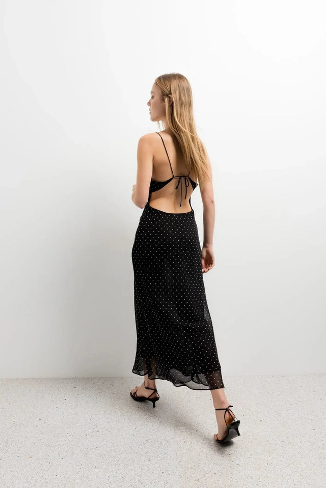 Vue arrière de la robe noire à pois blanc, la coupe fluide et le dos nu attirent l'œil, ajoutant un charme estival.