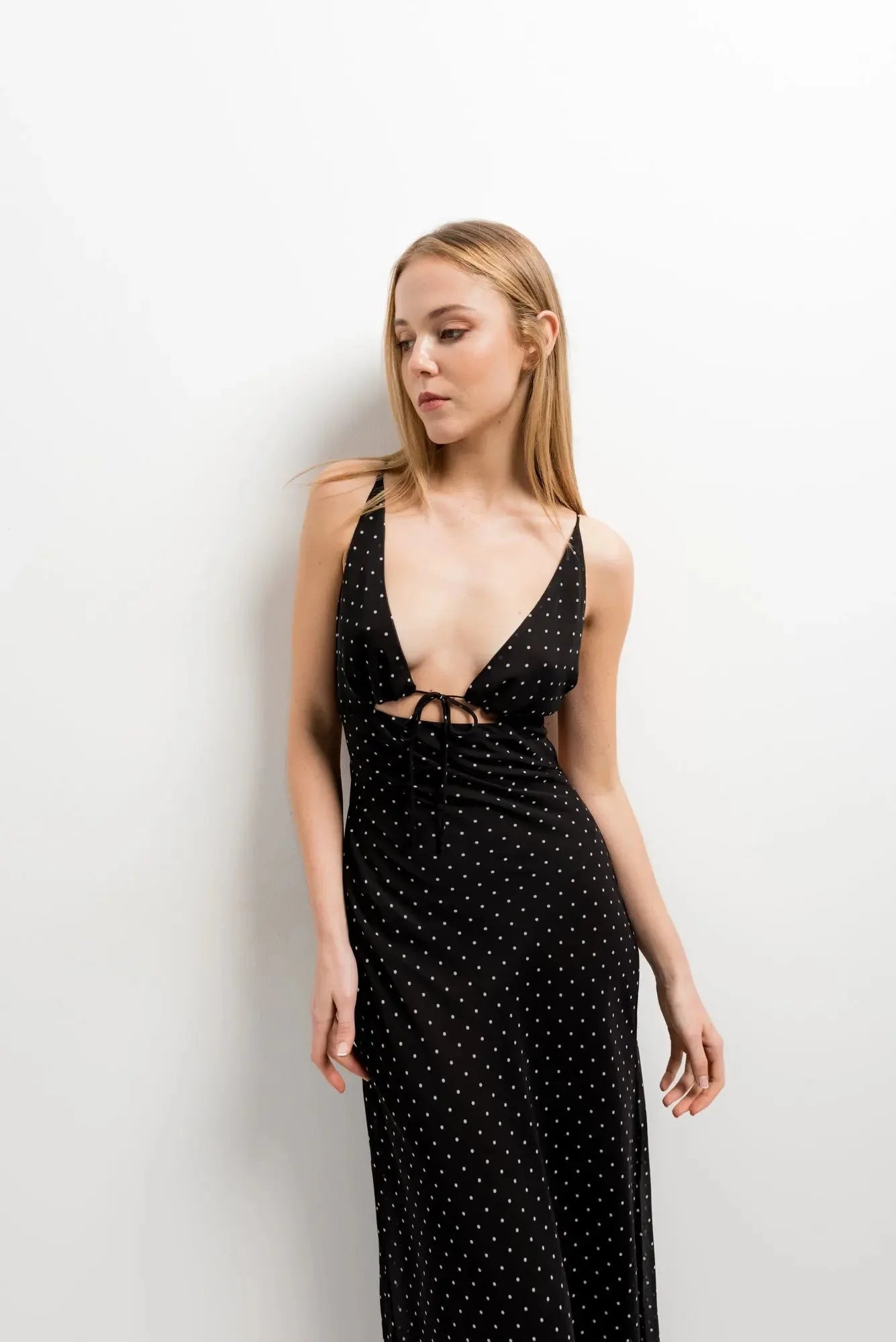 Modèle portant la robe noire à pois blanc, élégante et fluide, avec un décolleté plongeant et un dos nu, idéale pour des soirées estivales.