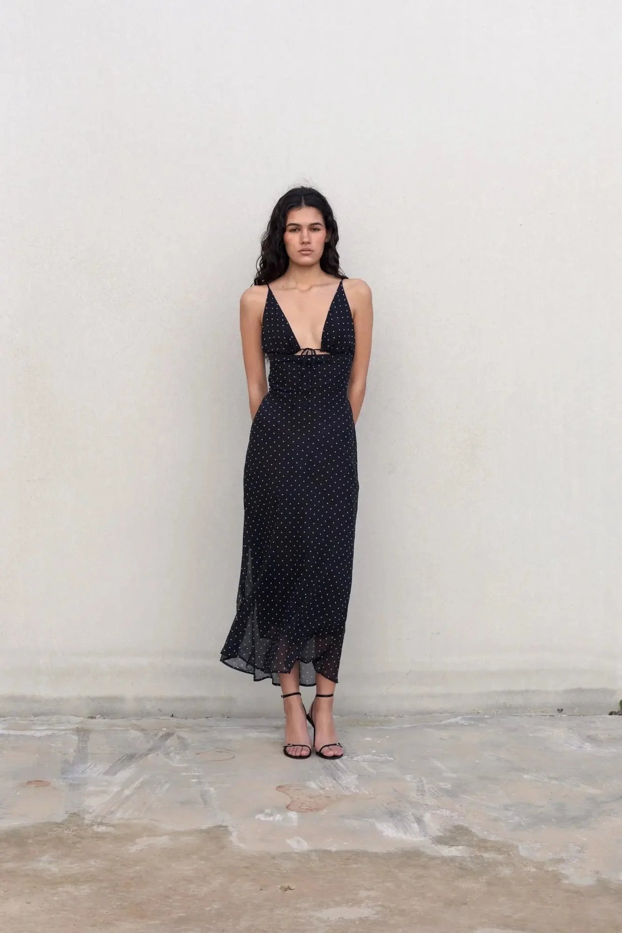 Femme posant dans la robe noire à pois blanc, soulignant la silhouette avec un style décontracté et élégant.