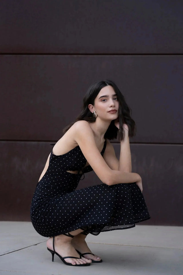 Femme assise dans une pose détendue, vêtue de la robe noire à pois blanc qui souligne la silhouette avec élégance.