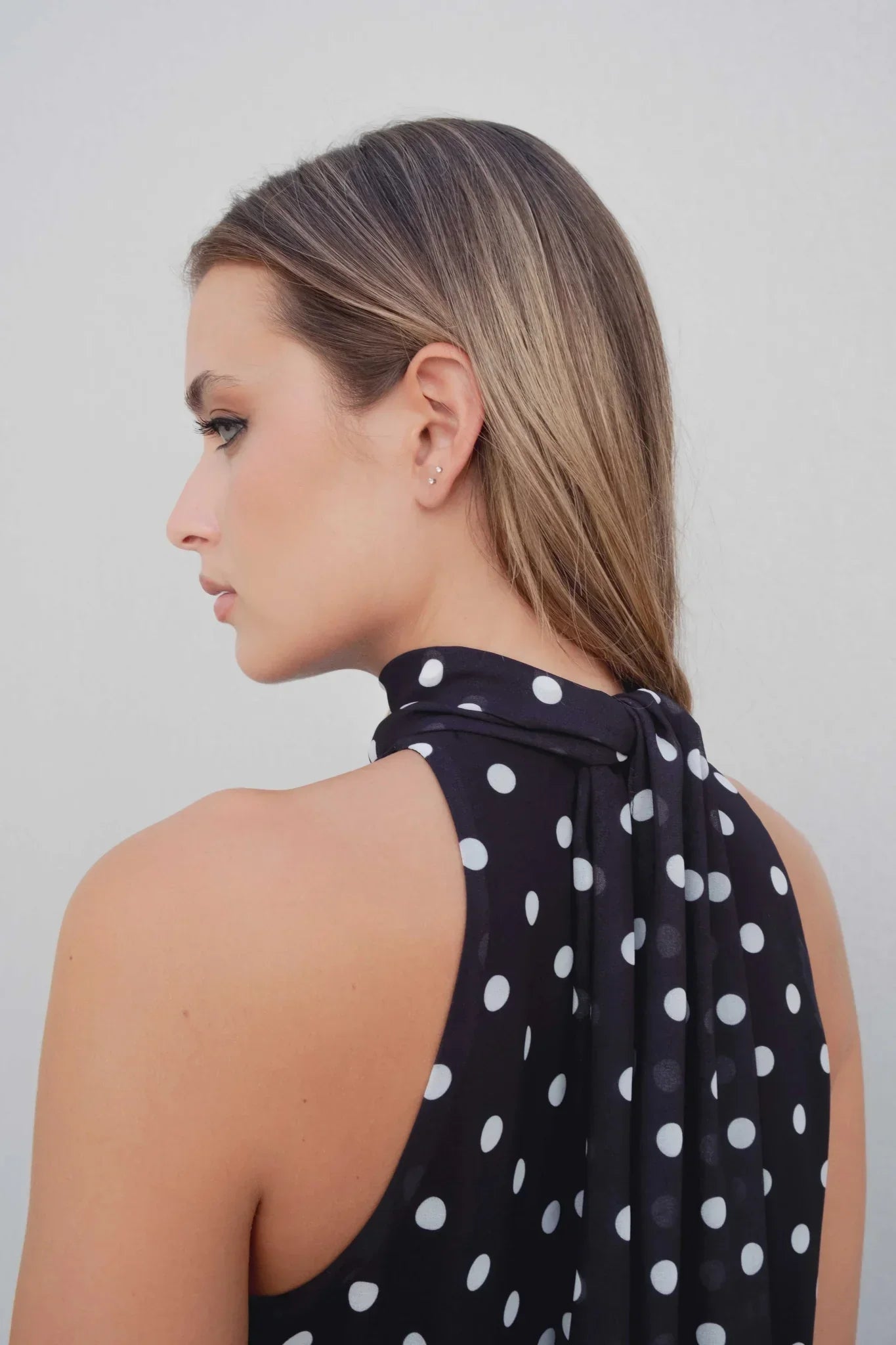 Femme portant une robe noire à pois blancs sans dos, haut à col montant