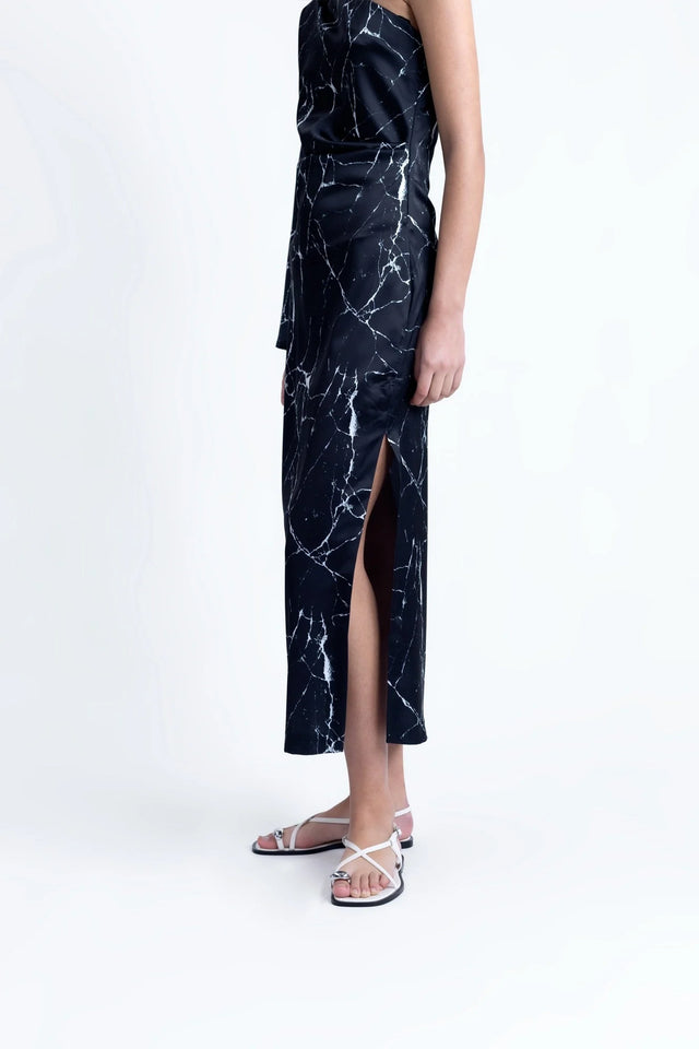 Zoom sur le bas de la Robe de Soirée Femme Asymétrique Satinée Noire Avec Imprimé Marbre, soulignant la fente et le tissu satiné.