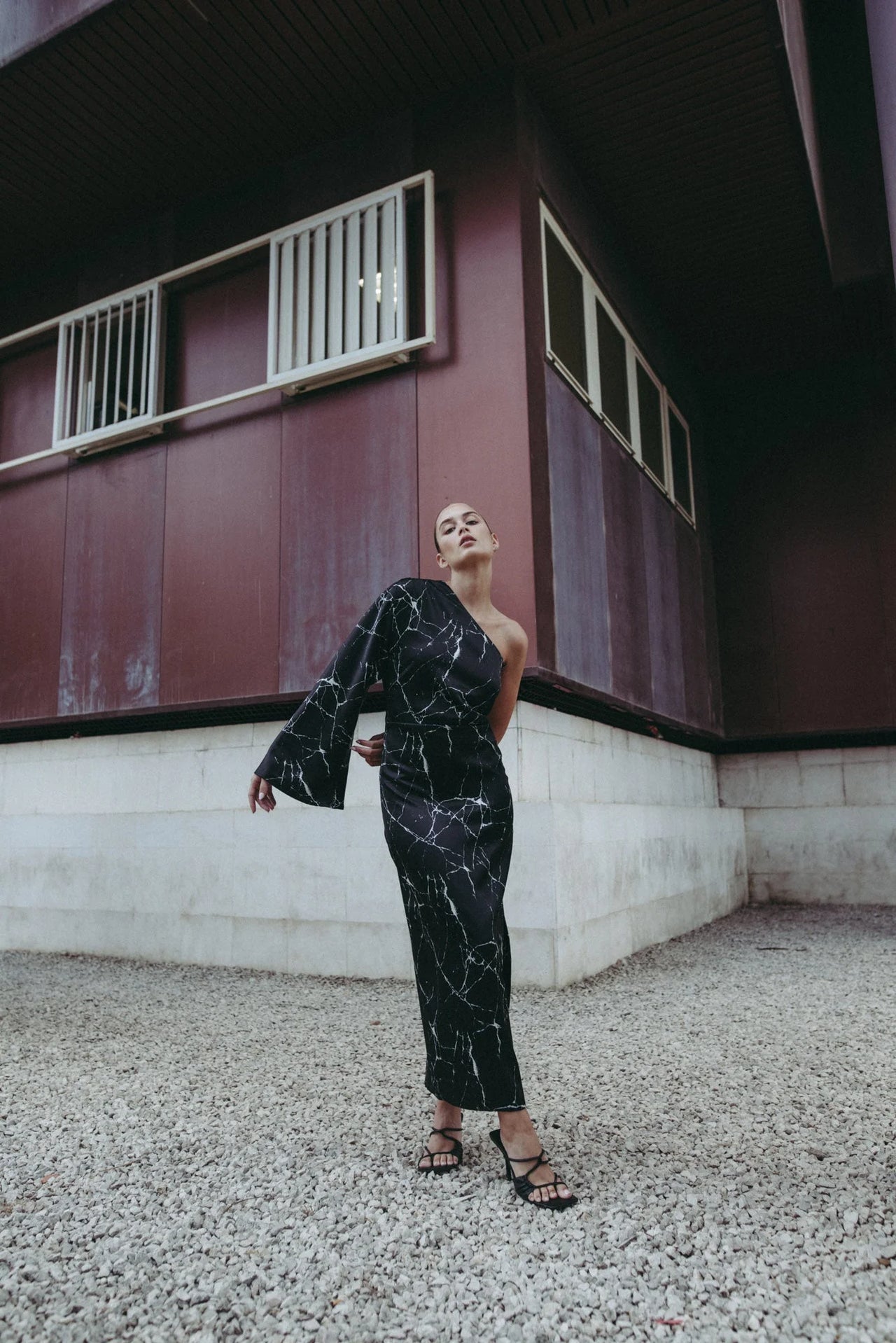 Femme posant en extérieur avec la Robe de Soirée Femme Asymétrique Satinée Noire Avec Imprimé Marbre, capturant le style et l'élégance.