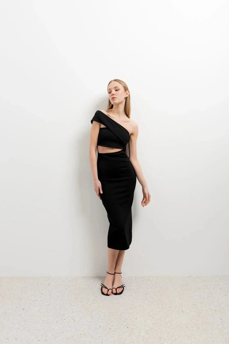 Vue de profil de la robe noire midi asymétrique découpée, style moderne avec un détail de taille ouvert, illustrant la tendance de la robe ouverte sur le côté.