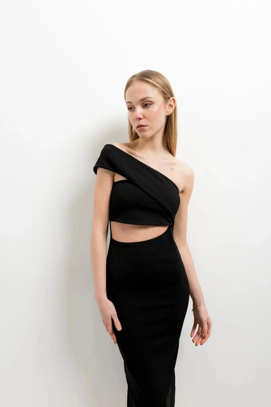 Portrait féminin portant la robe noire midi asymétrique découpée, mettant en avant le design élégant à une épaule et le style tendance de la robe ouverte sur le côté.