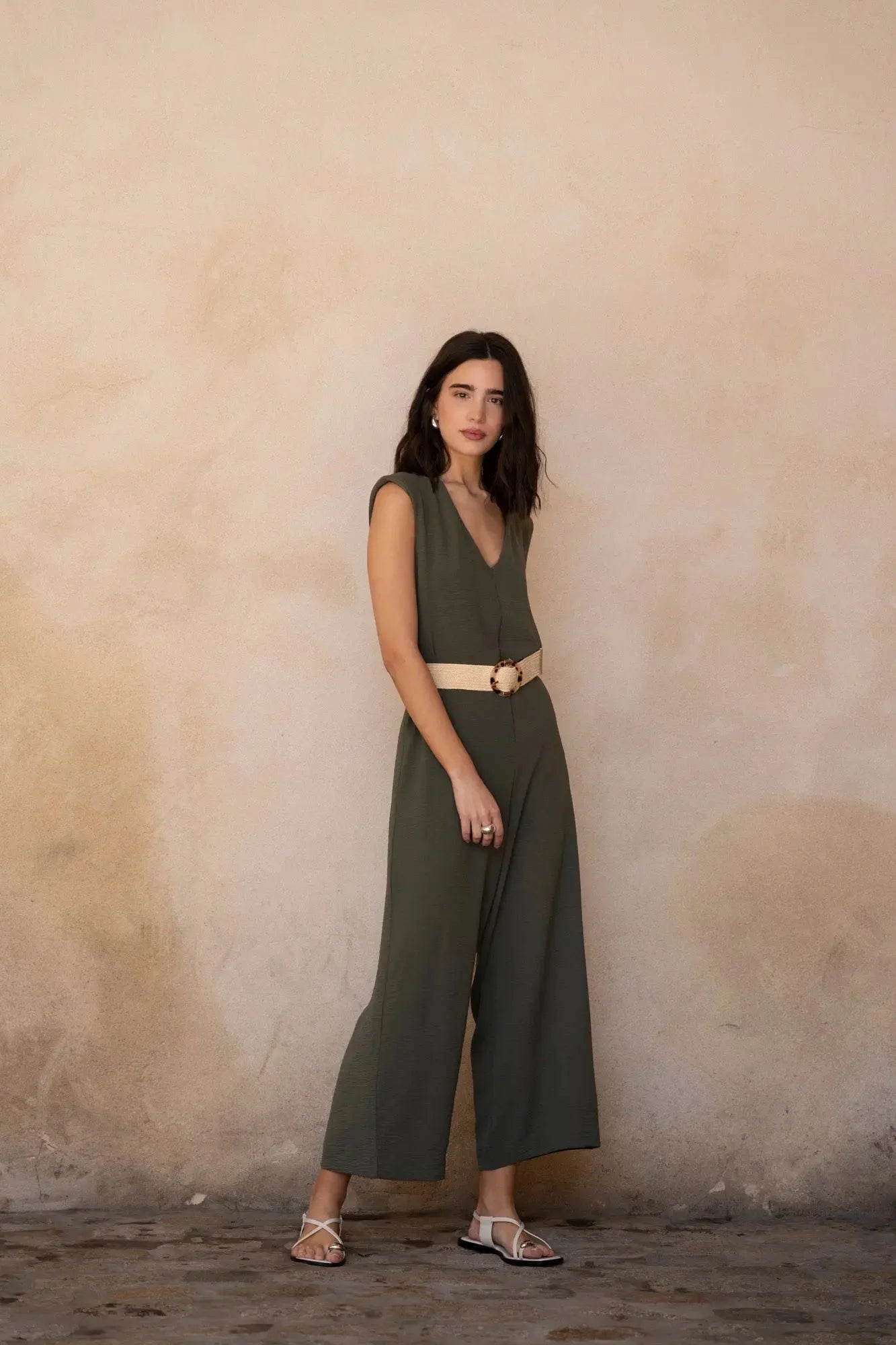 Femme portant robe pantalon vert foncé sans manches avec ceinture beige et sandales blanches