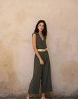 Femme debout dans une combinaison femme chic olive, sans manches, devant un mur beige, pour un look décontracté et élégant.
