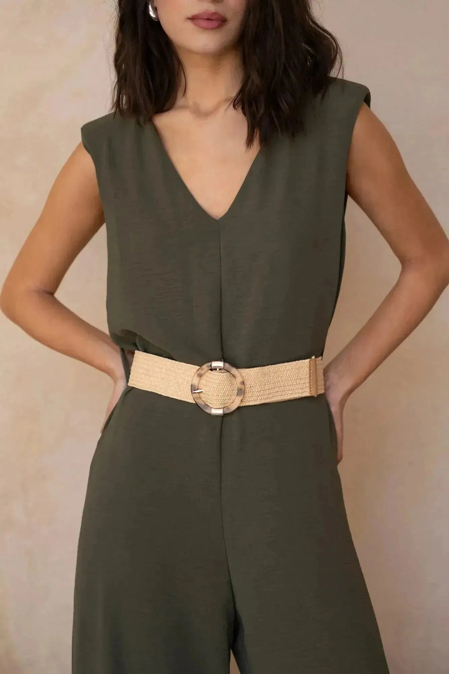 Gros plan sur une femme dans une combinaison femme chic olive, sans manches, accessorisé avec une ceinture, mettant en avant le col en V.