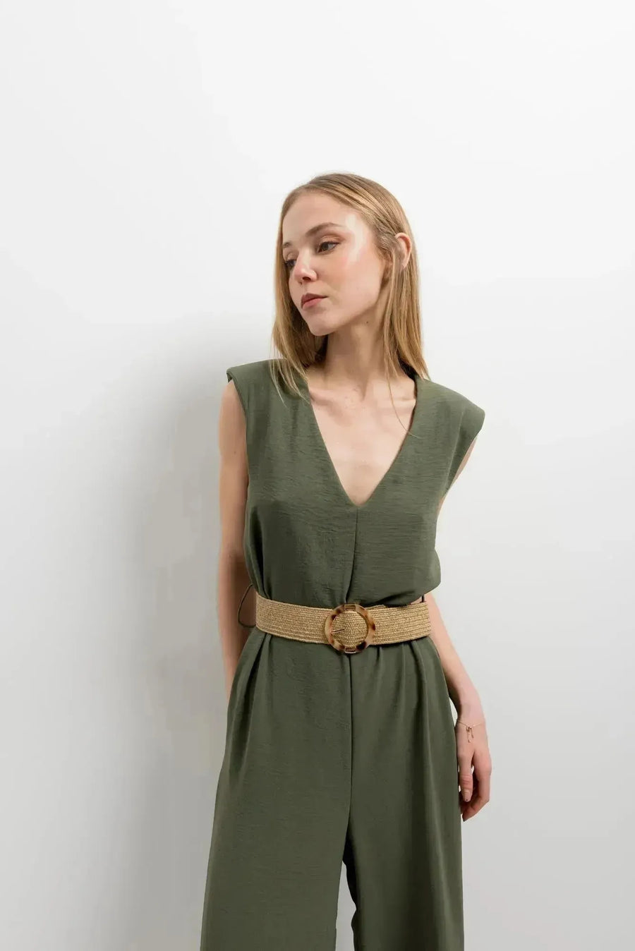Femme portant une combinaison femme chic olive, sans manches avec un col en V, mettant en valeur élégance et confort, ceinturée avec une ceinture en jute.
