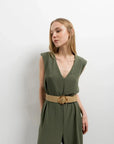 Femme portant une combinaison femme chic olive, sans manches avec un col en V, mettant en valeur élégance et confort, ceinturée avec une ceinture en jute.