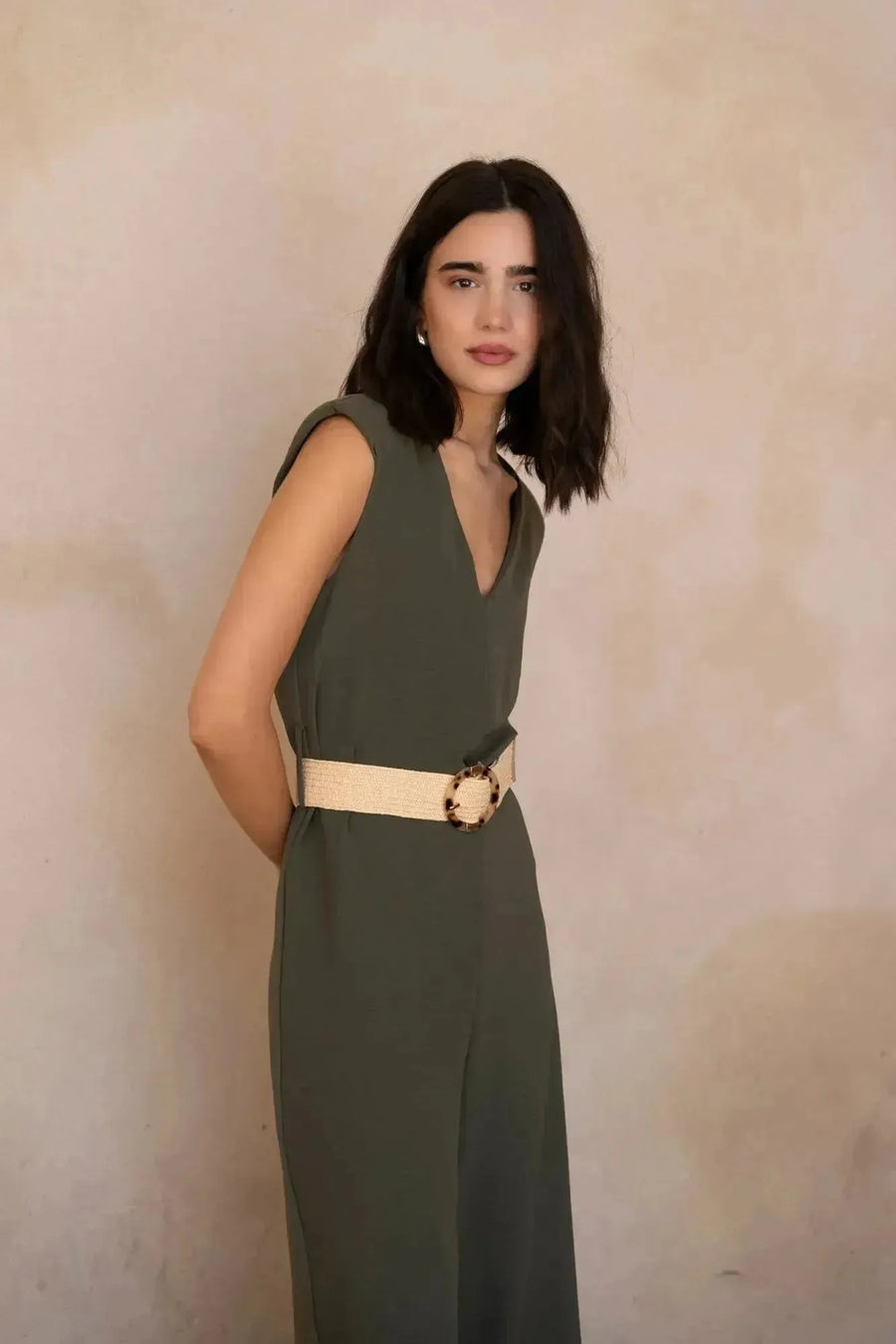 Femme souriante dans une combinaison femme chic olive, sans manches, avec ceinture, affichant un style élégant et tendance.