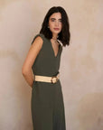 Femme souriante dans une combinaison femme chic olive, sans manches, avec ceinture, affichant un style élégant et tendance.