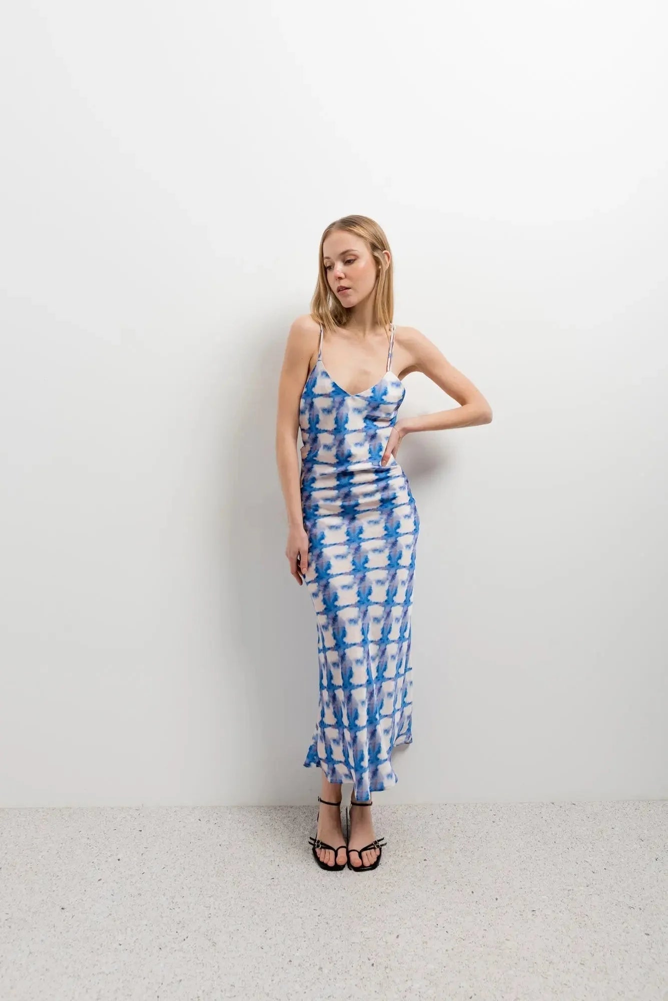 Femme dans une robe tie and dye bleue midi à bretelles fines, posant avec une allure chic parfaite pour les journées d'été.
