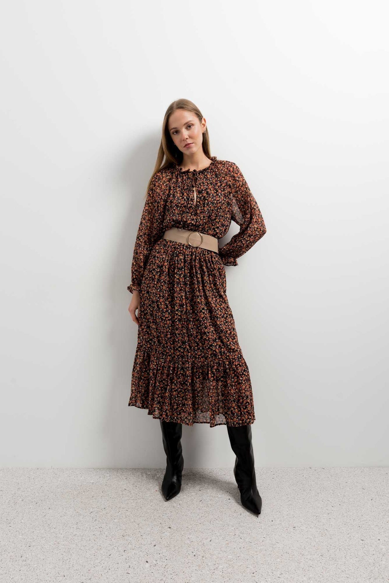 Femme posant dans une robe ample imprimée fleurie longue noire avec ceinture cintrée légère, parfaite pour toutes les occasions. Robe ample, robe fleurie longue, robe avec ceinture.