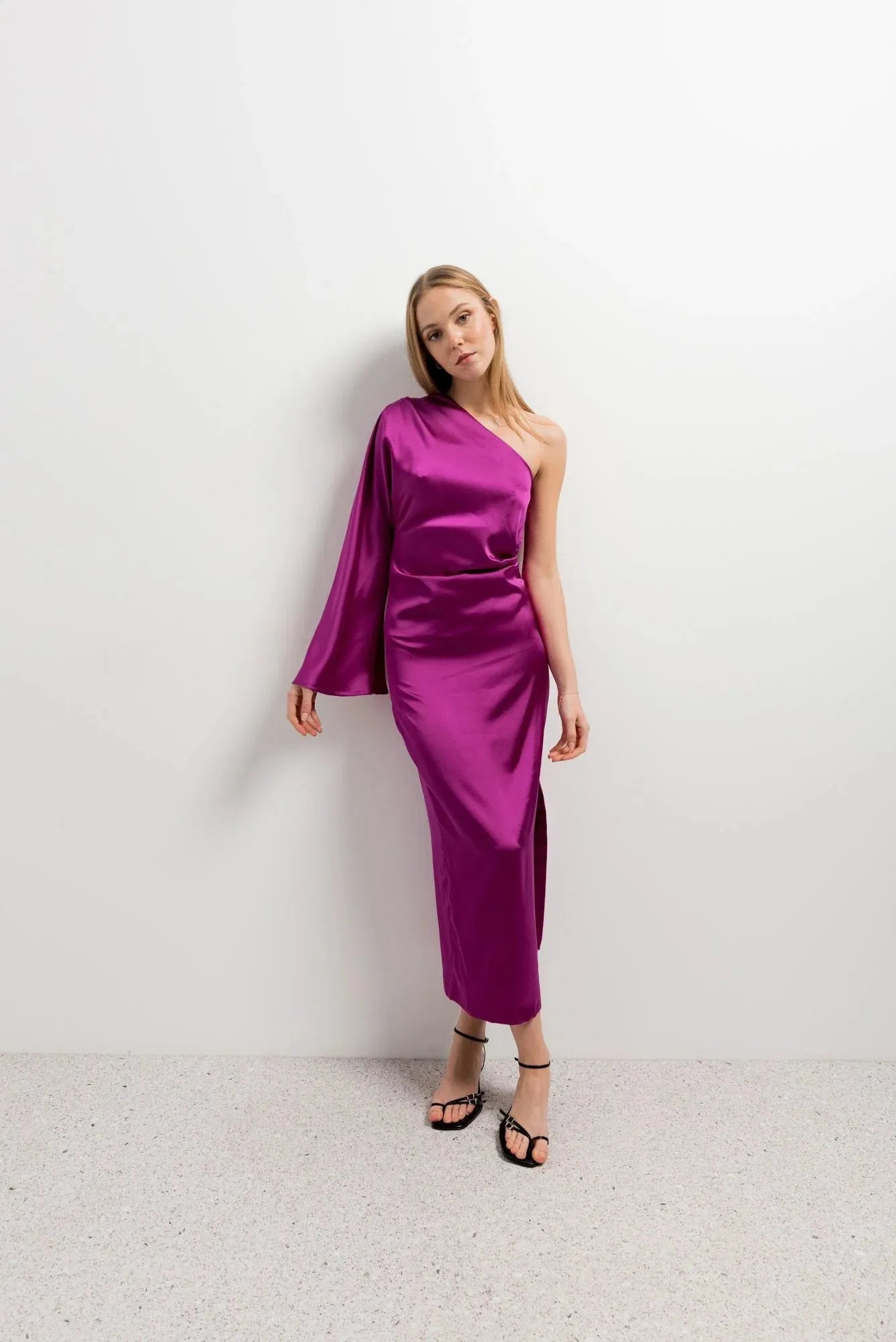 Modèle portant la robe midi asymétrique rose fuchsia en satin à une épaule, parfaite pour une soirée élégante. Idéale comme robe asymétrique de soirée.