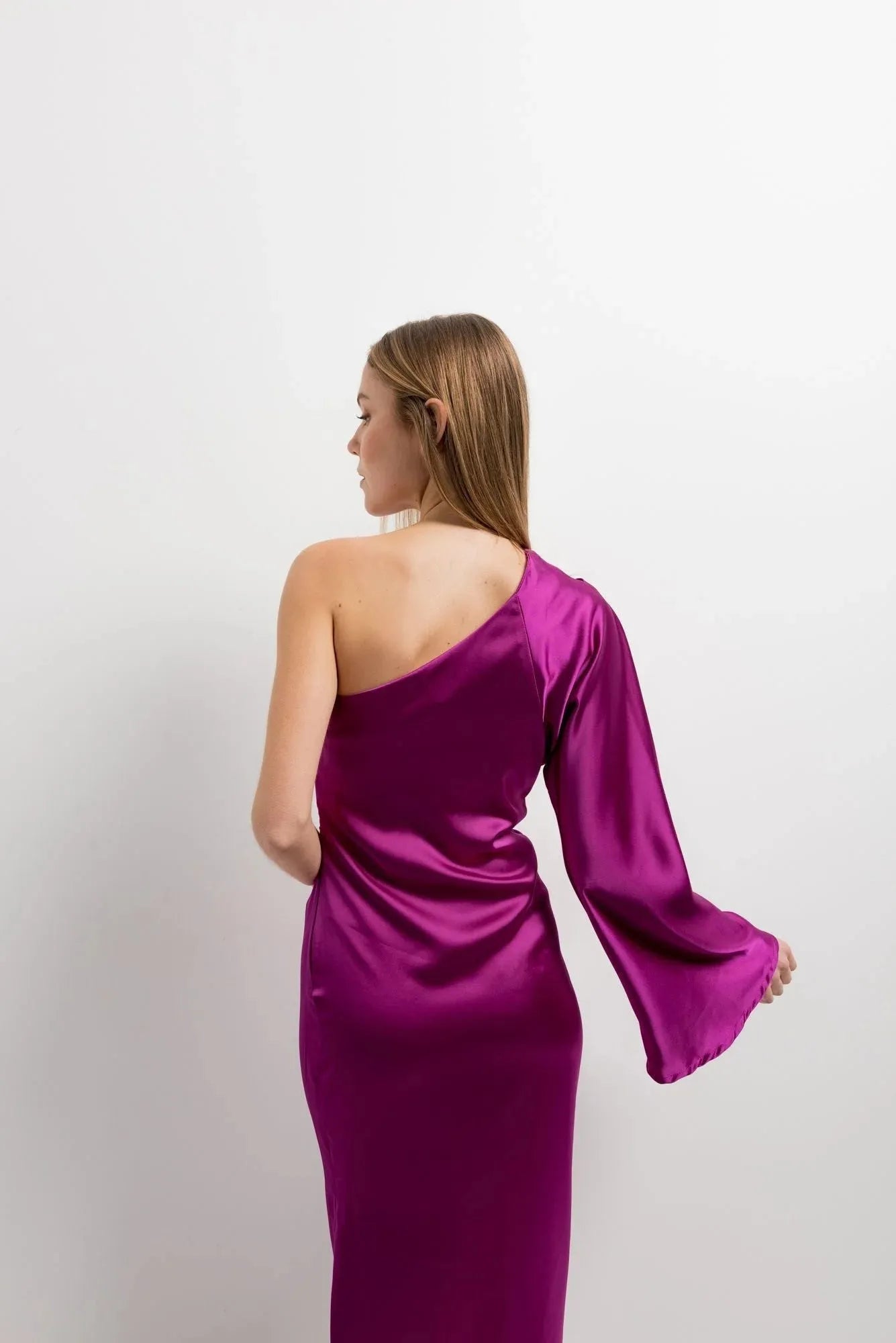 Vue arrière d'un modèle portant la robe midi asymétrique rose fuchsia en satin à une épaule, alliant sophistication et confort. Optez pour cette robe asymétrique de soirée.