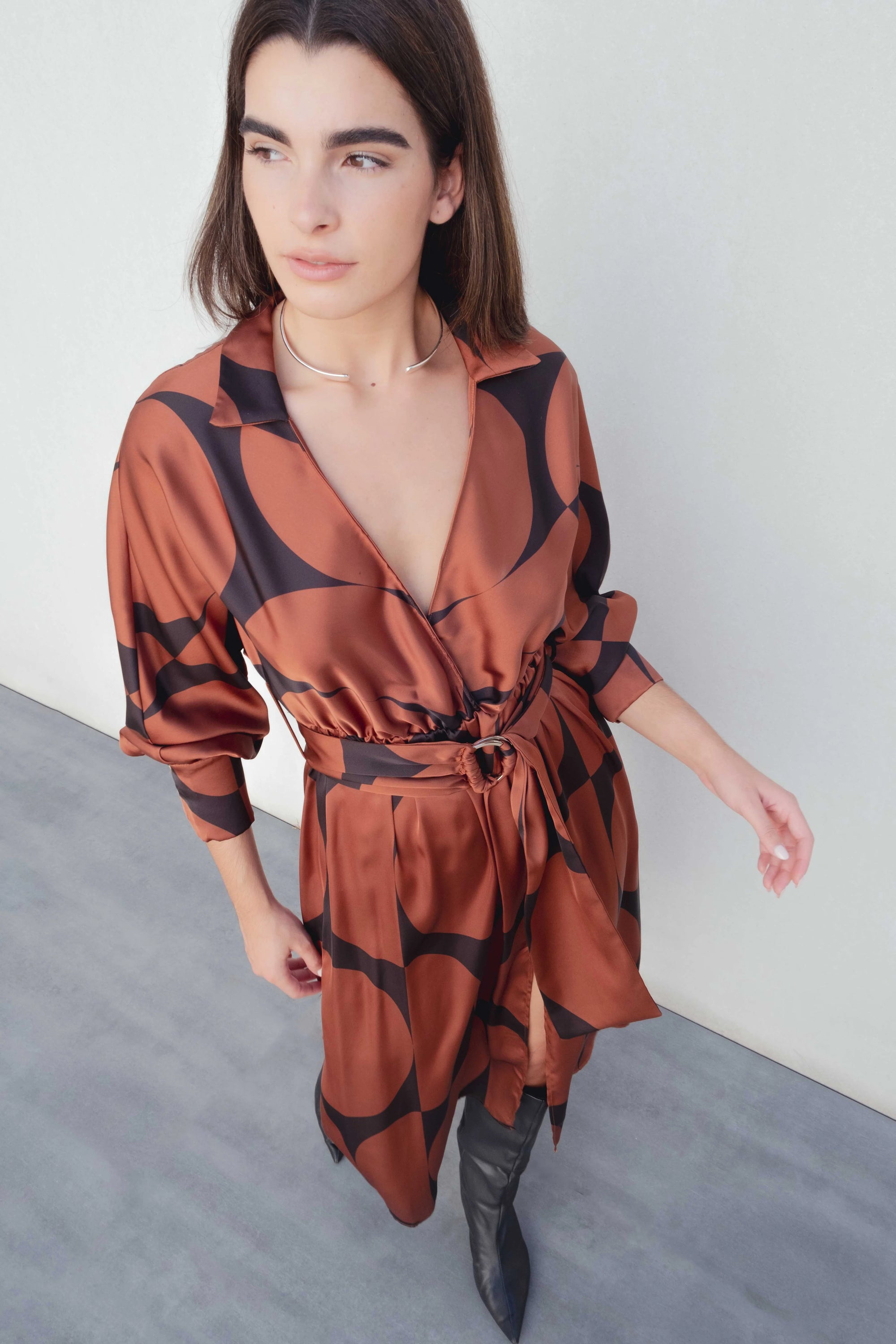 Femme posant avec assurance dans la Robe Portefeuille Femme À Imprimé Géométrique Noir & Marron, avec un environnement moderne.