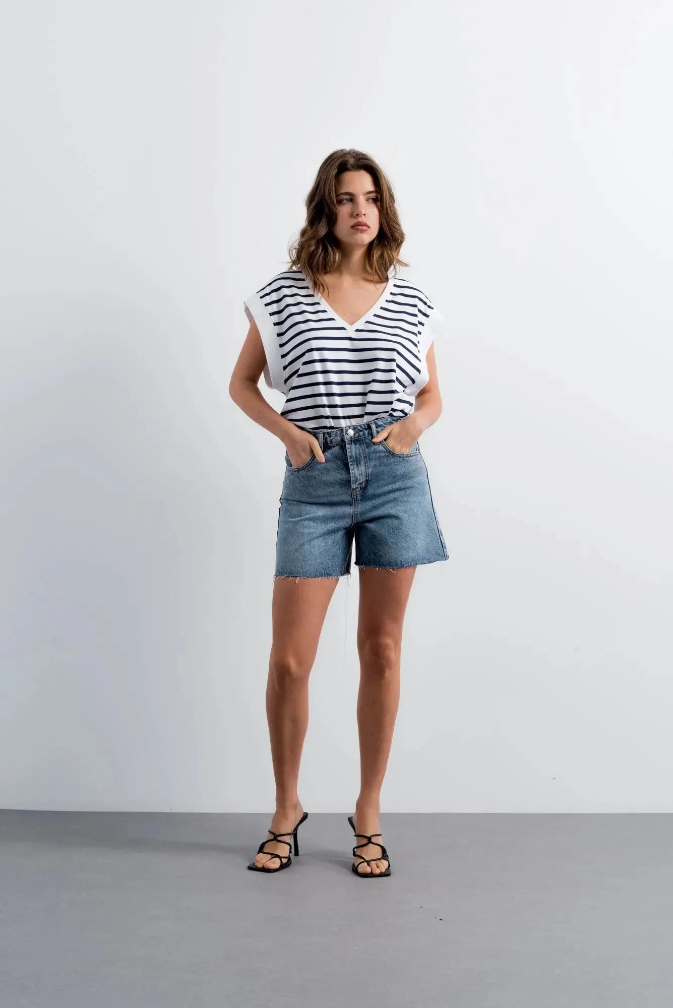 Femme portant shorts en jean style bermuda chic, top rayé blanc et navy, sandales noires