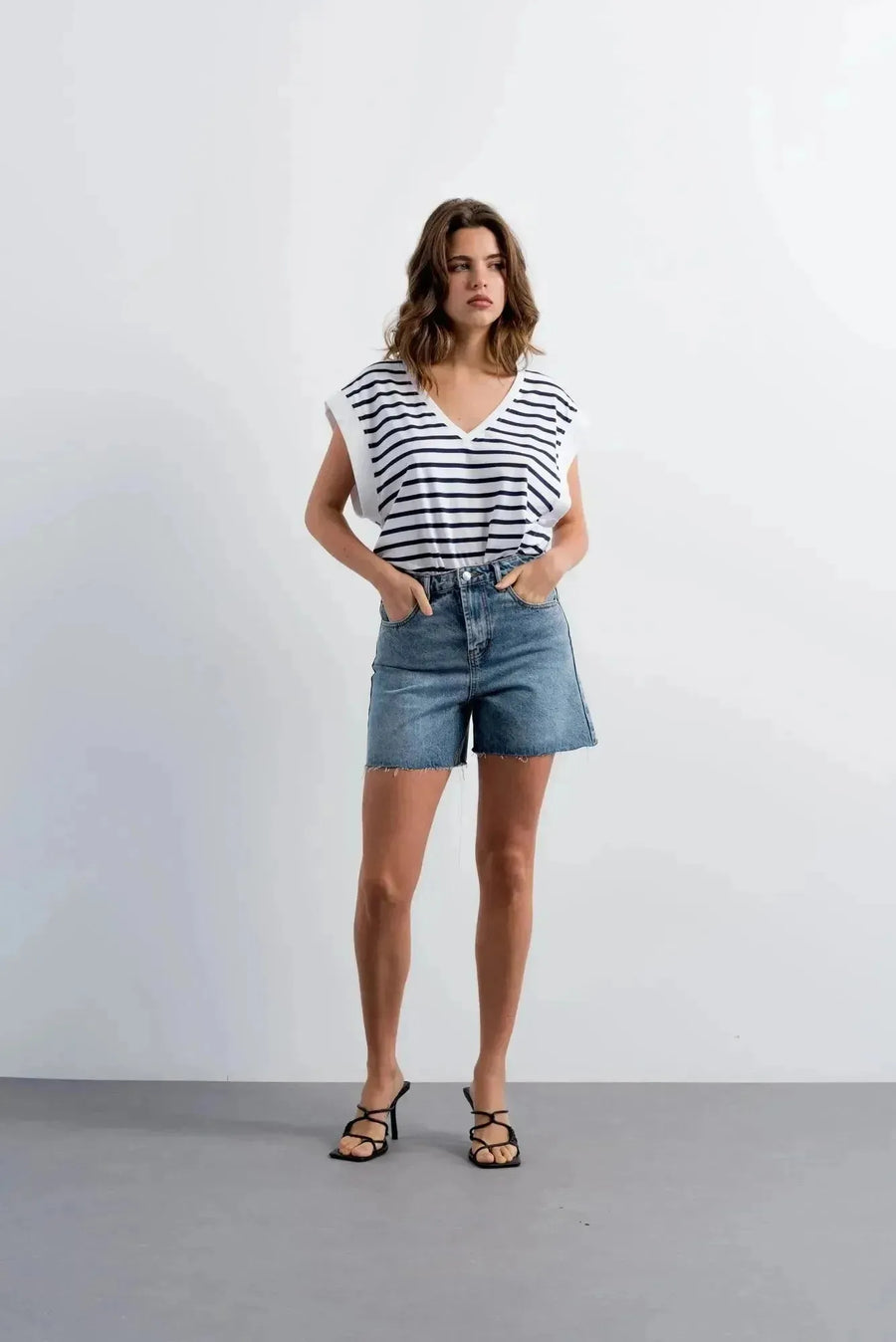 Femme portant shorts en jean style bermuda chic, top rayé blanc et navy, sandales noires