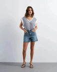 Femme portant shorts en jean style bermuda chic, top rayé blanc et navy, sandales noires
