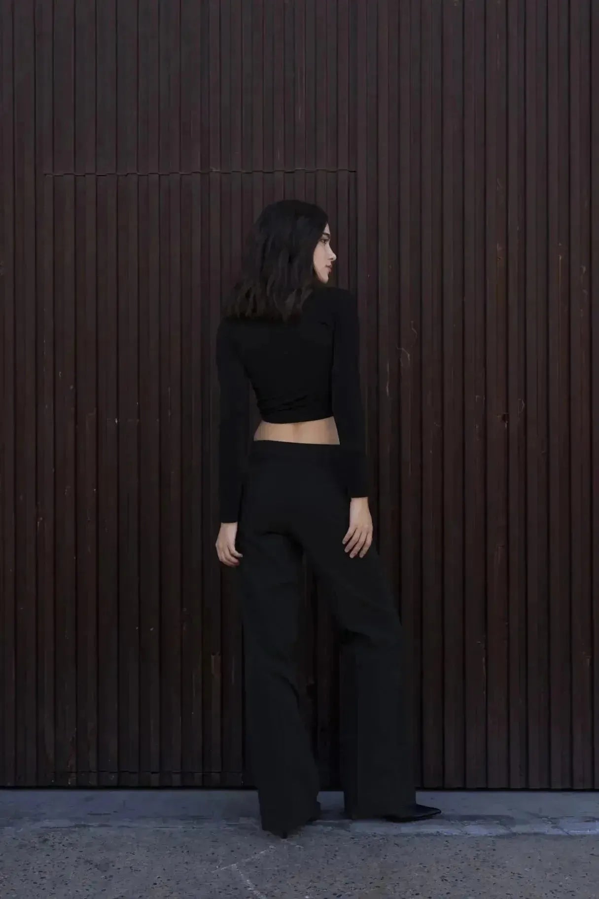 Vue arrière d'une femme en T-Shirt Crop Top Manche Longue Avec Noeud Élégant Pour Femme, combiné avec des pantalons élégants pour un look moderne.