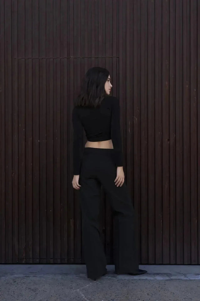 Vue arrière d'une femme en T-Shirt Crop Top Manche Longue Avec Noeud Élégant Pour Femme, combiné avec des pantalons élégants pour un look moderne.