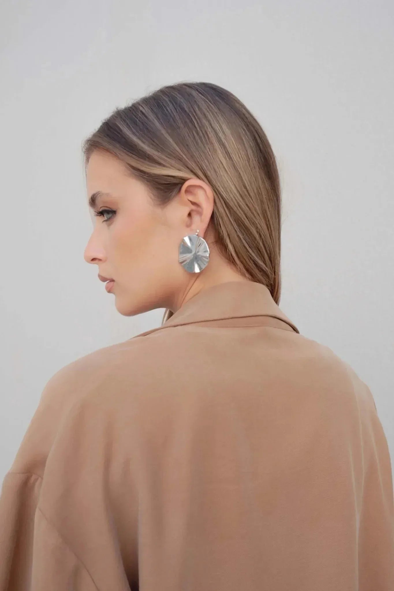 Vue de profil d'une femme en blazer fluide camel avec des boucles d'oreilles modernes.